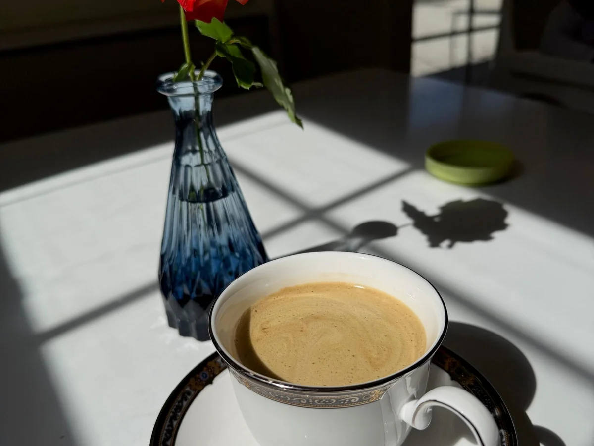 Red rose in blue glass vase beside coffee cup on white table