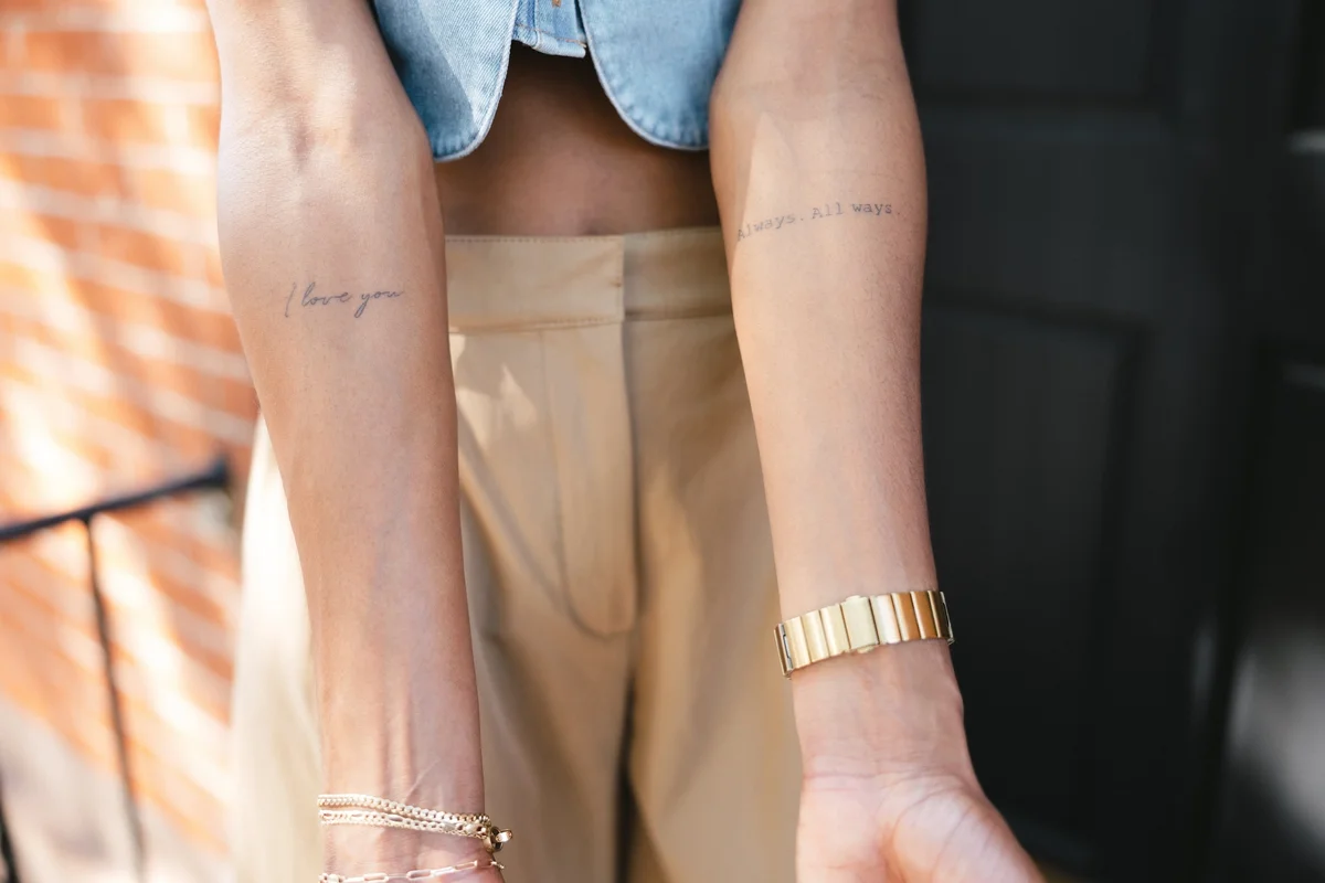 Woman's arms with small script tattoos and gold jewelry