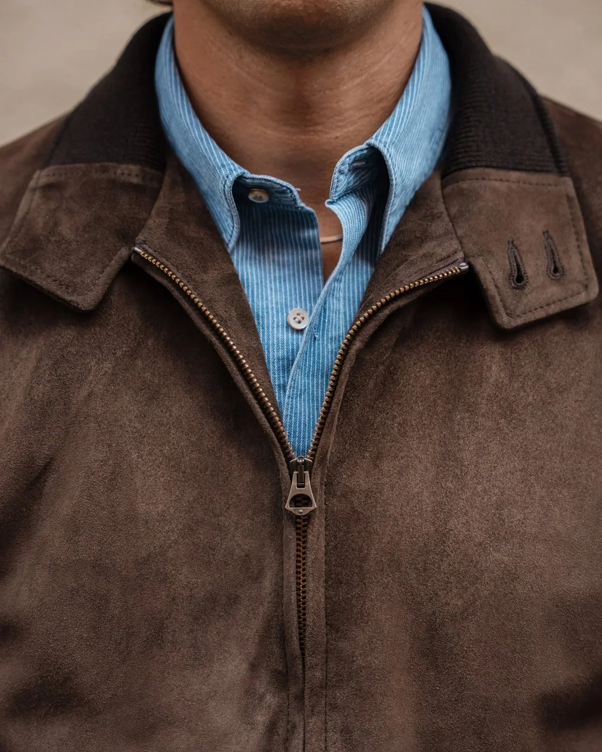 Close-up of a brown suede jacket worn over a striped shirt