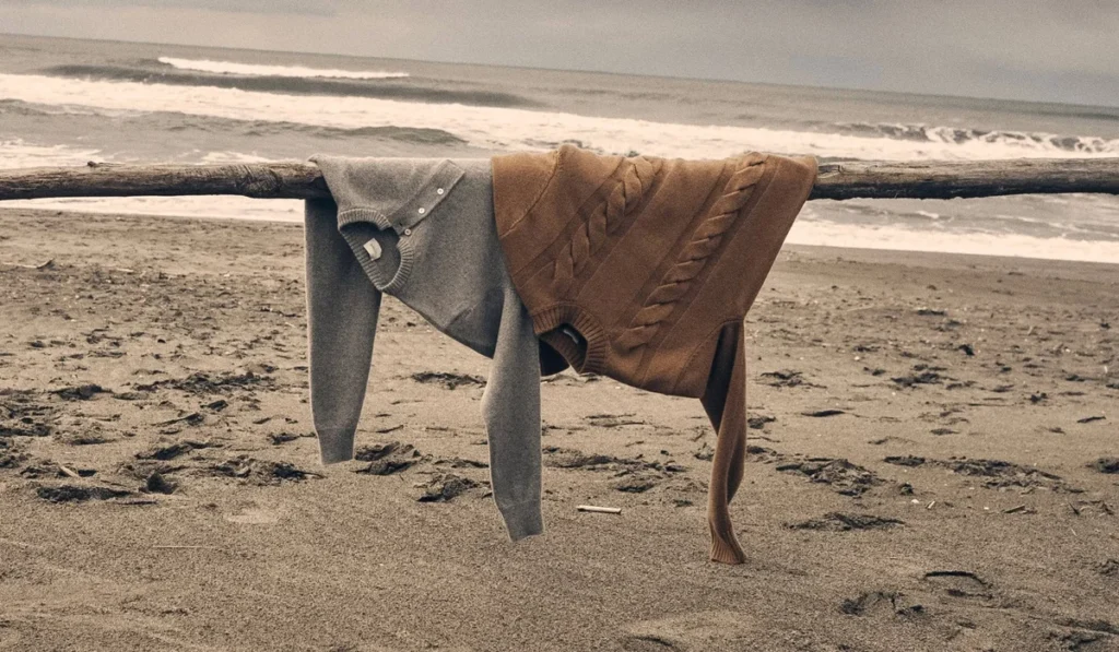 Two luxury knit sweaters resting on driftwood by the sea