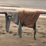 Two luxury knit sweaters resting on driftwood by the sea