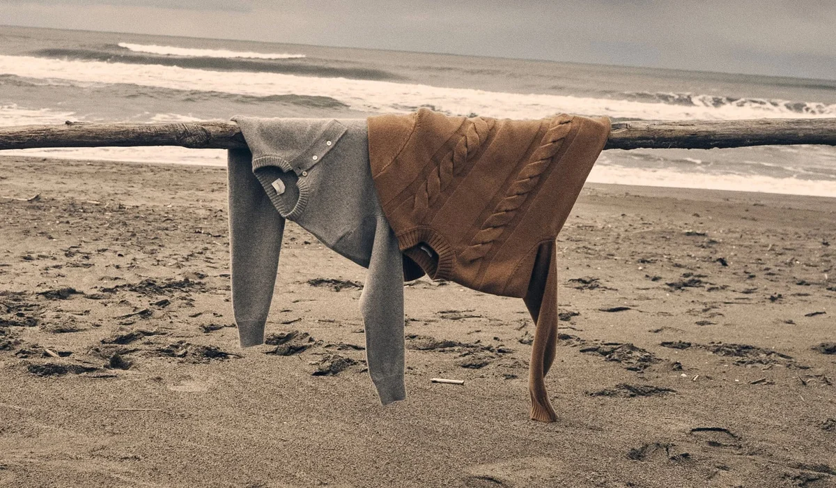 Two luxury knit sweaters resting on driftwood by the sea