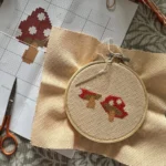 Cross-stitch toadstool embroidery in progress on linen fabric